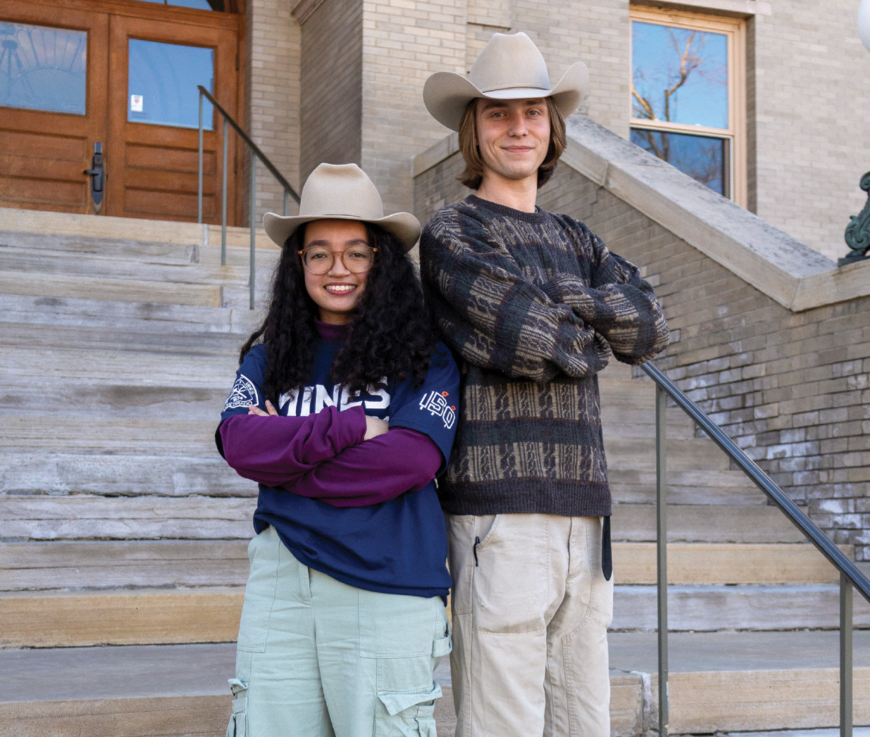 Two Mines students posing in The Mines Hat in front of Guggenheim Hall.